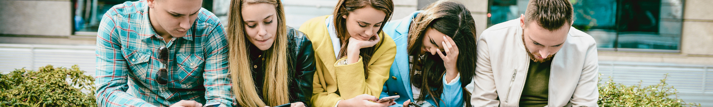 Ein Foto von 5 Jugendlichen, die an der frischen Luft sitzen aber alle auf ihr Handy schauen.